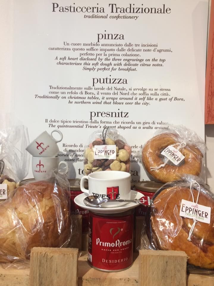 Esposizione di dolci italiani con descrizioni scritte a mano; include una tazza da caffè e prodotti in scatola.
