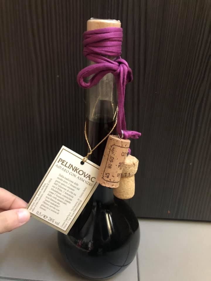 Una bottiglia di liquore scuro Pelinkovac con tappo di sughero, etichetta e nastro viola.