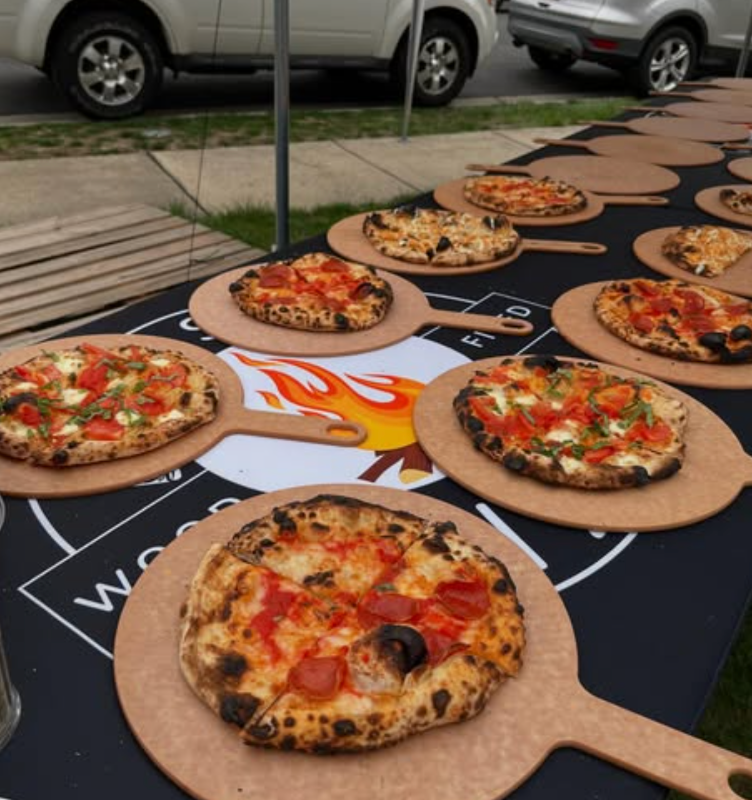 Pizzas on wooden serving boards, set out on a table under a white tent, ready to eat.