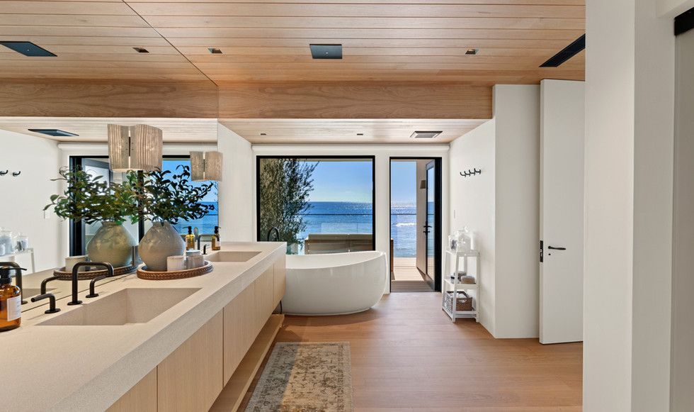 A bathroom with two sinks , a tub and a view of the ocean.