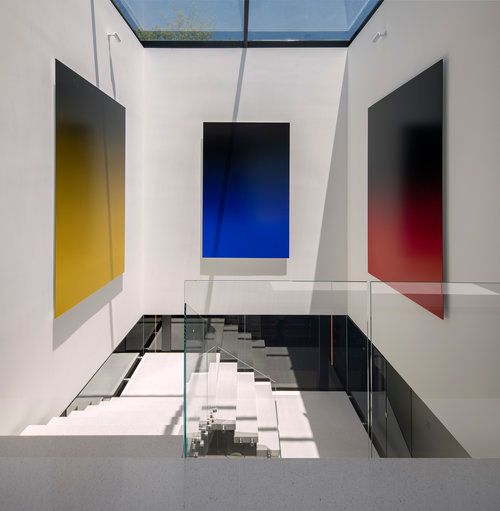 A staircase with a glass railing and three paintings on the wall