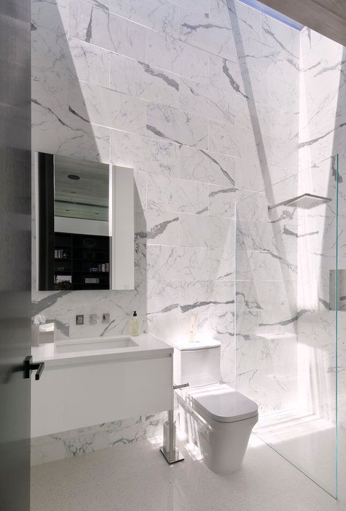 A bathroom with marble walls , a toilet , sink and mirror.