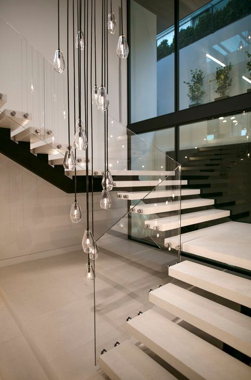 A modern staircase with a glass railing and lights hanging from the ceiling