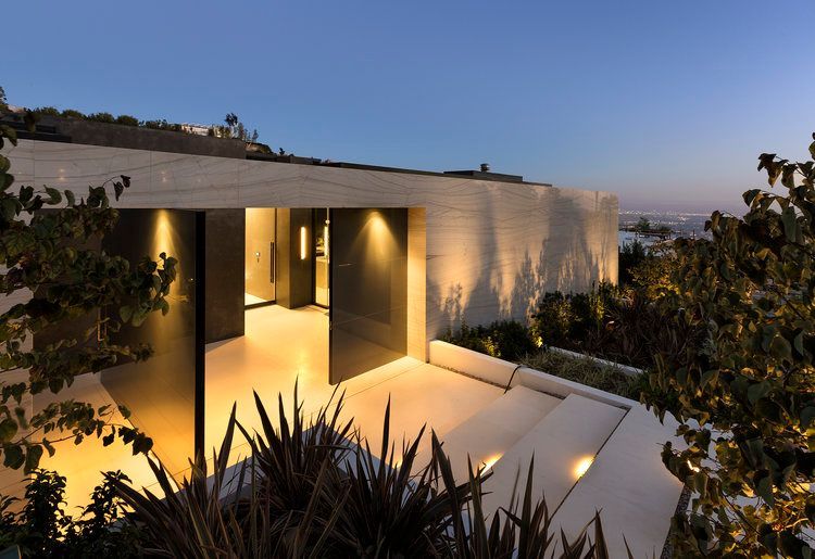A modern house is lit up at night with a view of the ocean.