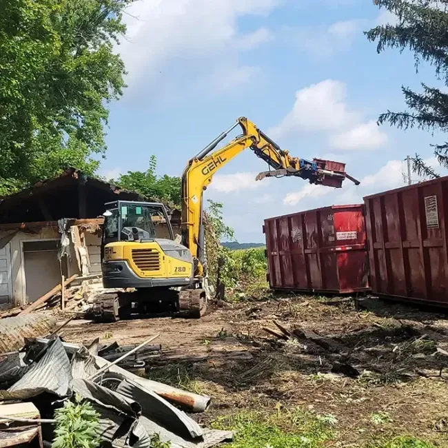 Excavator demolishing a concrete structure amid rubble under a cloudy sky