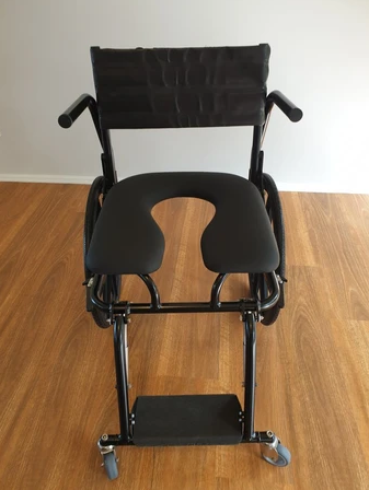 Black shower chair with a U-shaped seat, armrests, footrest, and wheels.