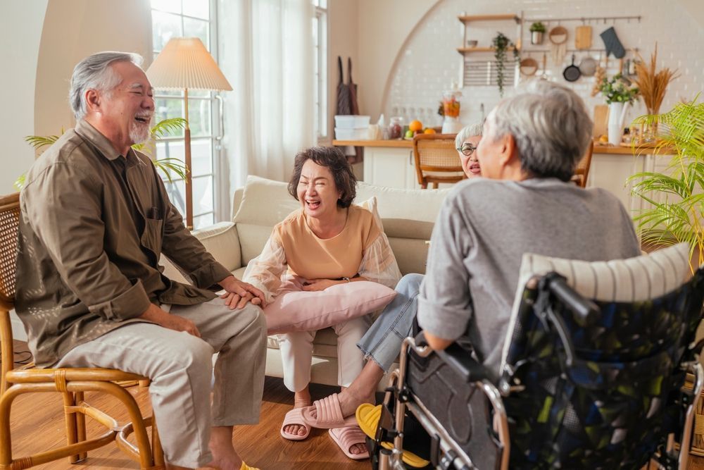 Group of elderly people laughing together in a living room; one in wheelchair.