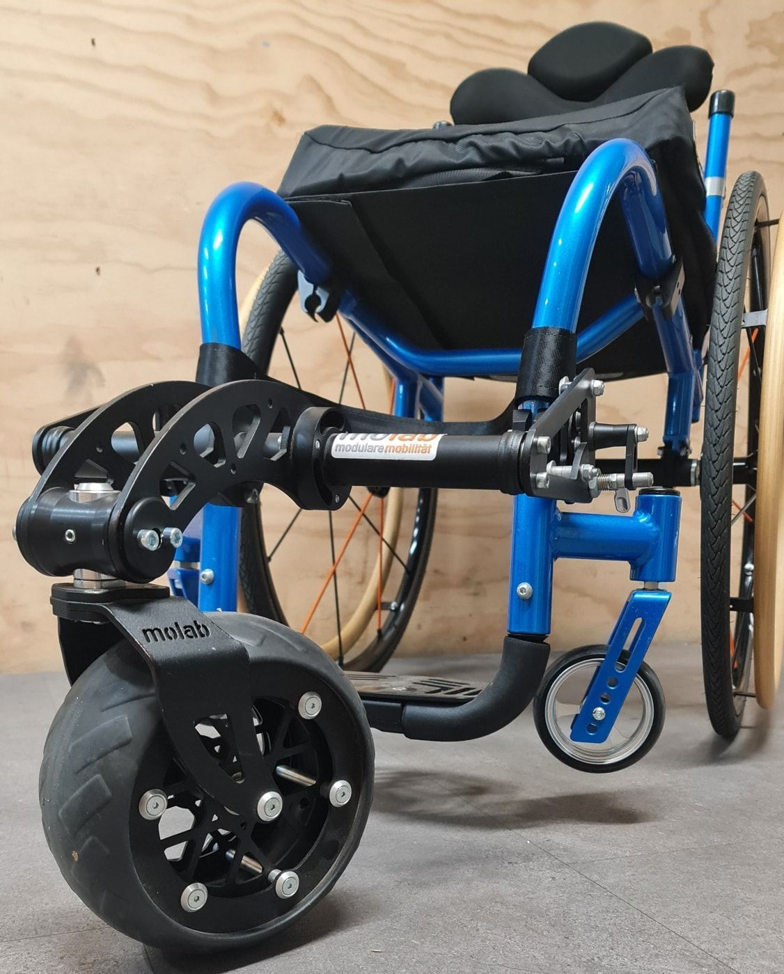 Blue and black wheelchair with large front wheels for navigating rough terrain.
