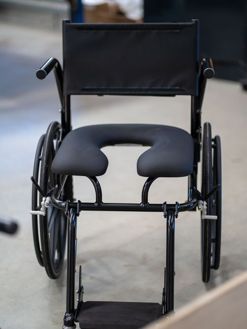 Black wheelchair with a U-shaped seat, positioned in an indoor setting.