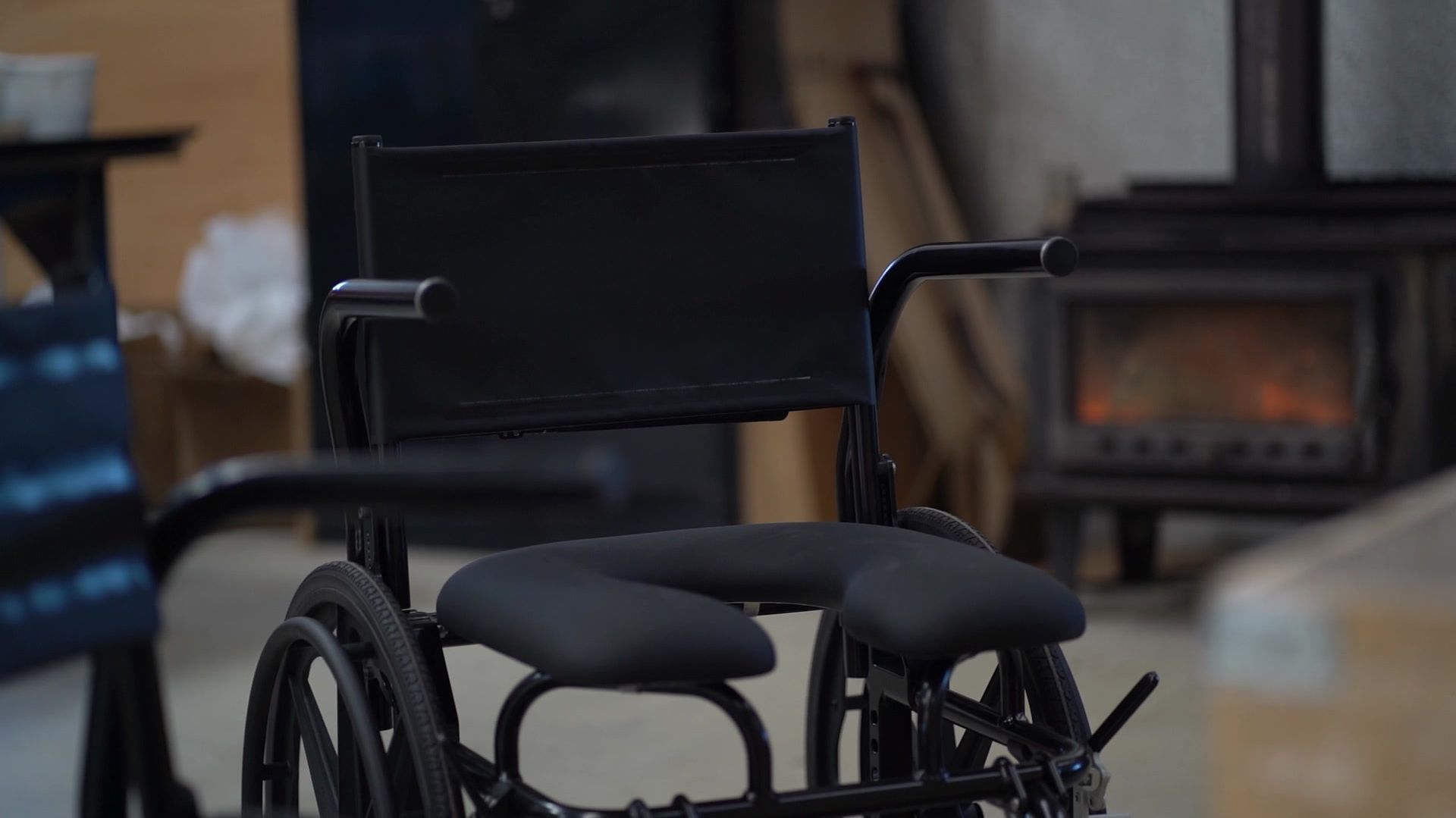 Black wheelchair with a cushioned seat, in front of a fireplace.