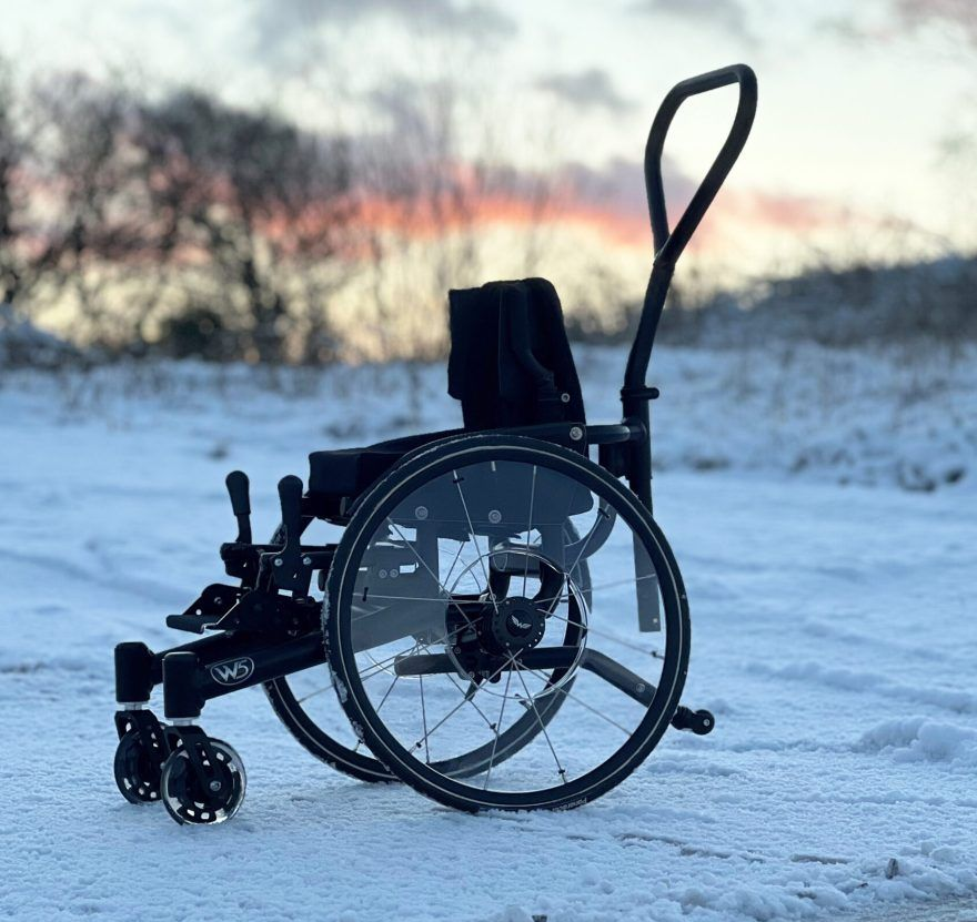 Black wheelchair on snow-covered ground with a sunset in the background.