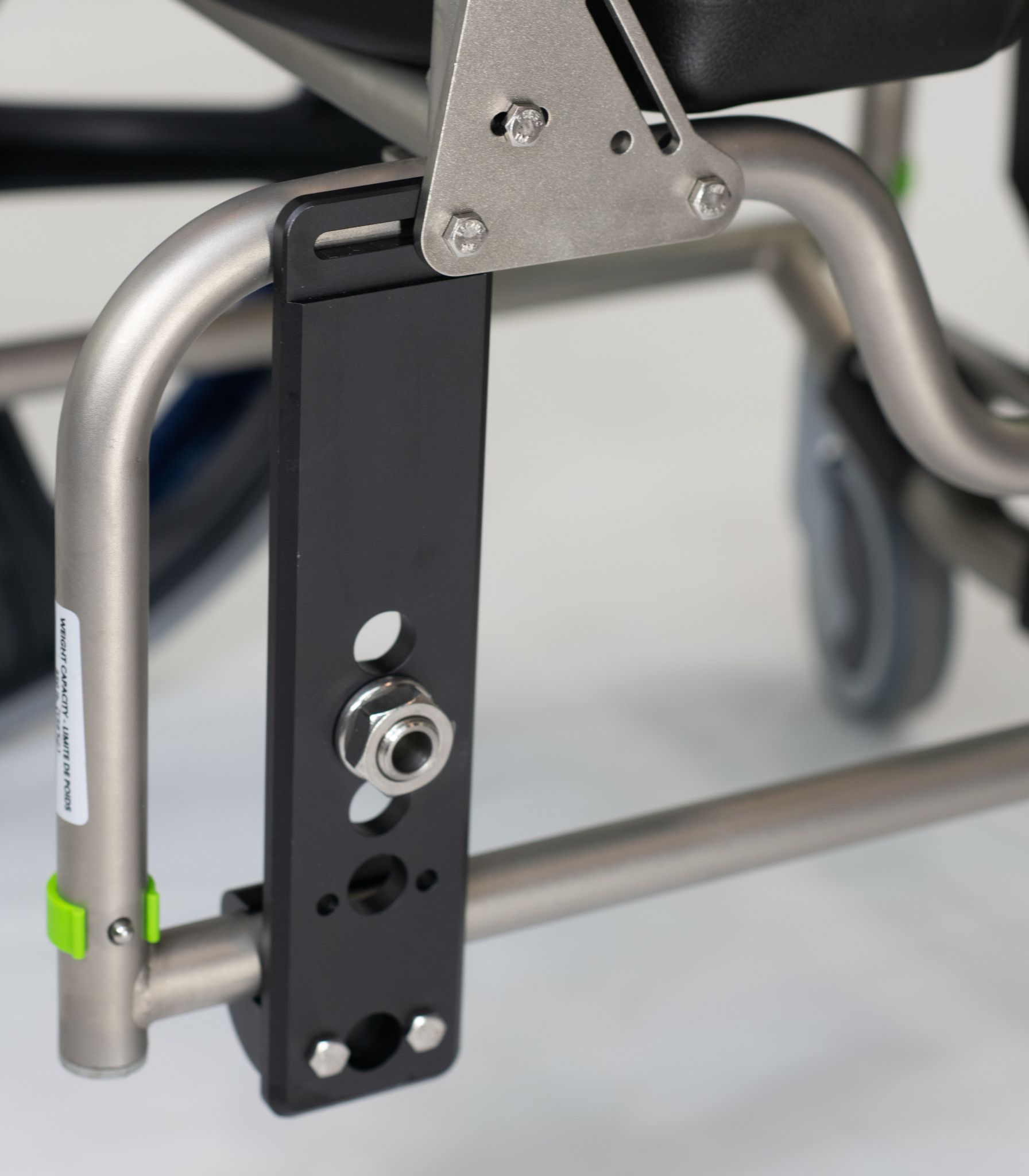 Close-up of a wheelchair's frame and black bracket with hardware attached to a metallic leg.