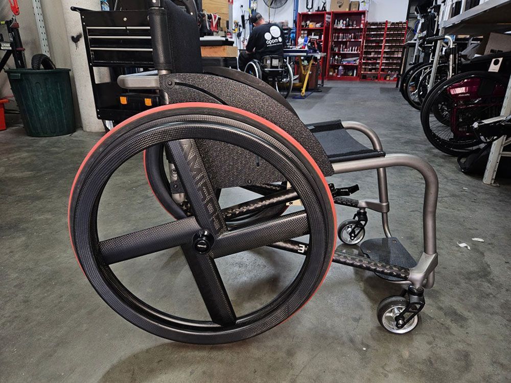 Wheelchair with black wheels and red tires, indoors.
