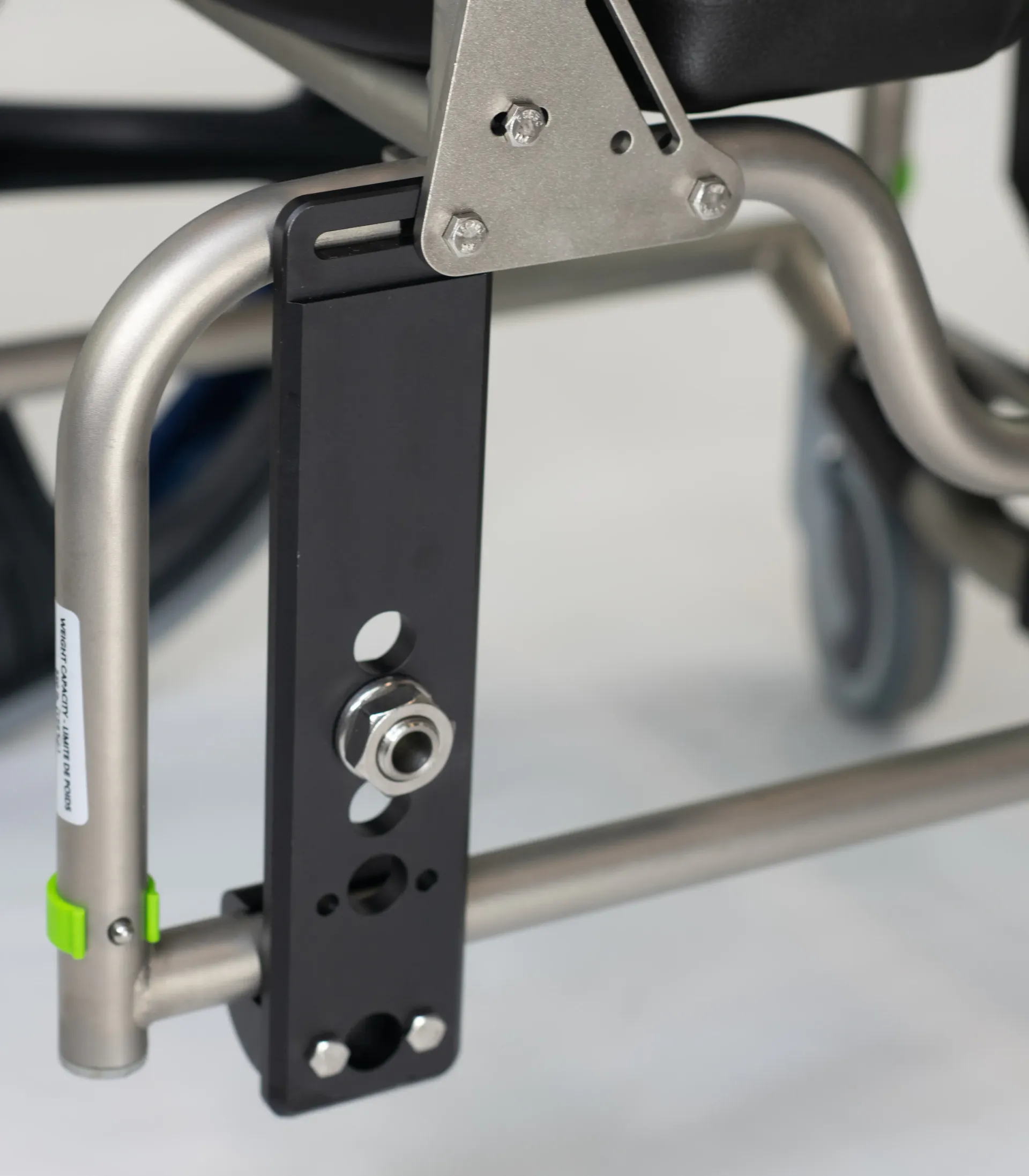 Close-up of a wheelchair component, showing a black bracket attached to the frame with bolts and screws.