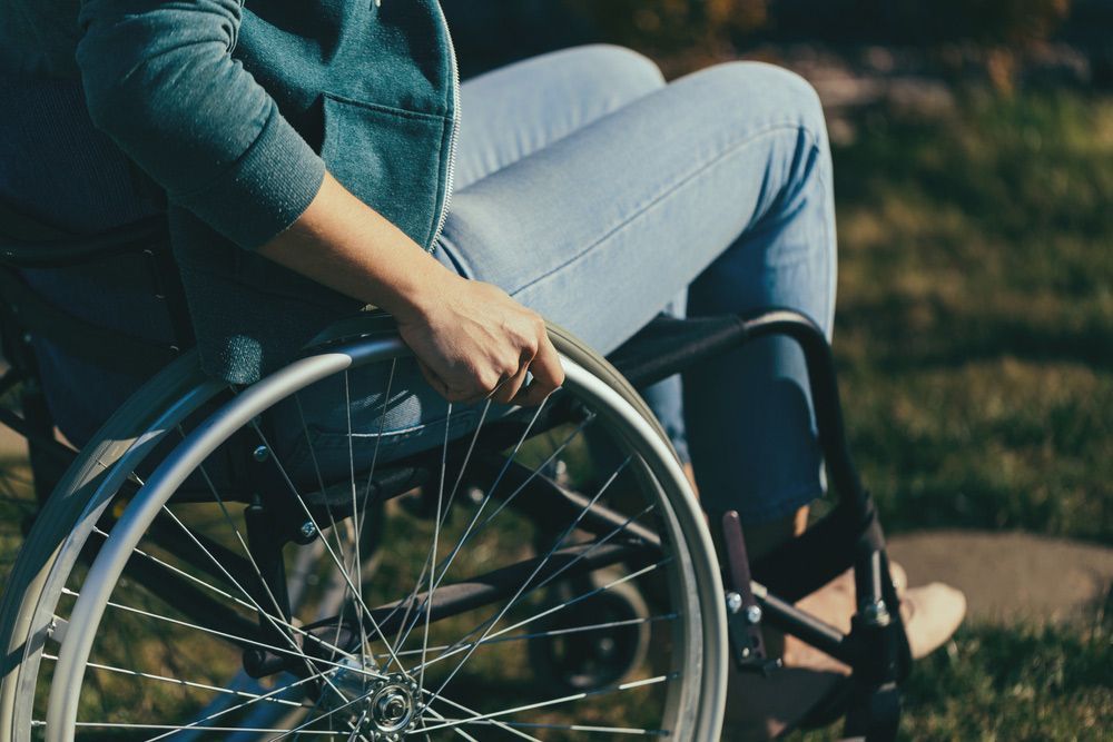 Person in a wheelchair outdoors, hand on the wheel, moving forward.