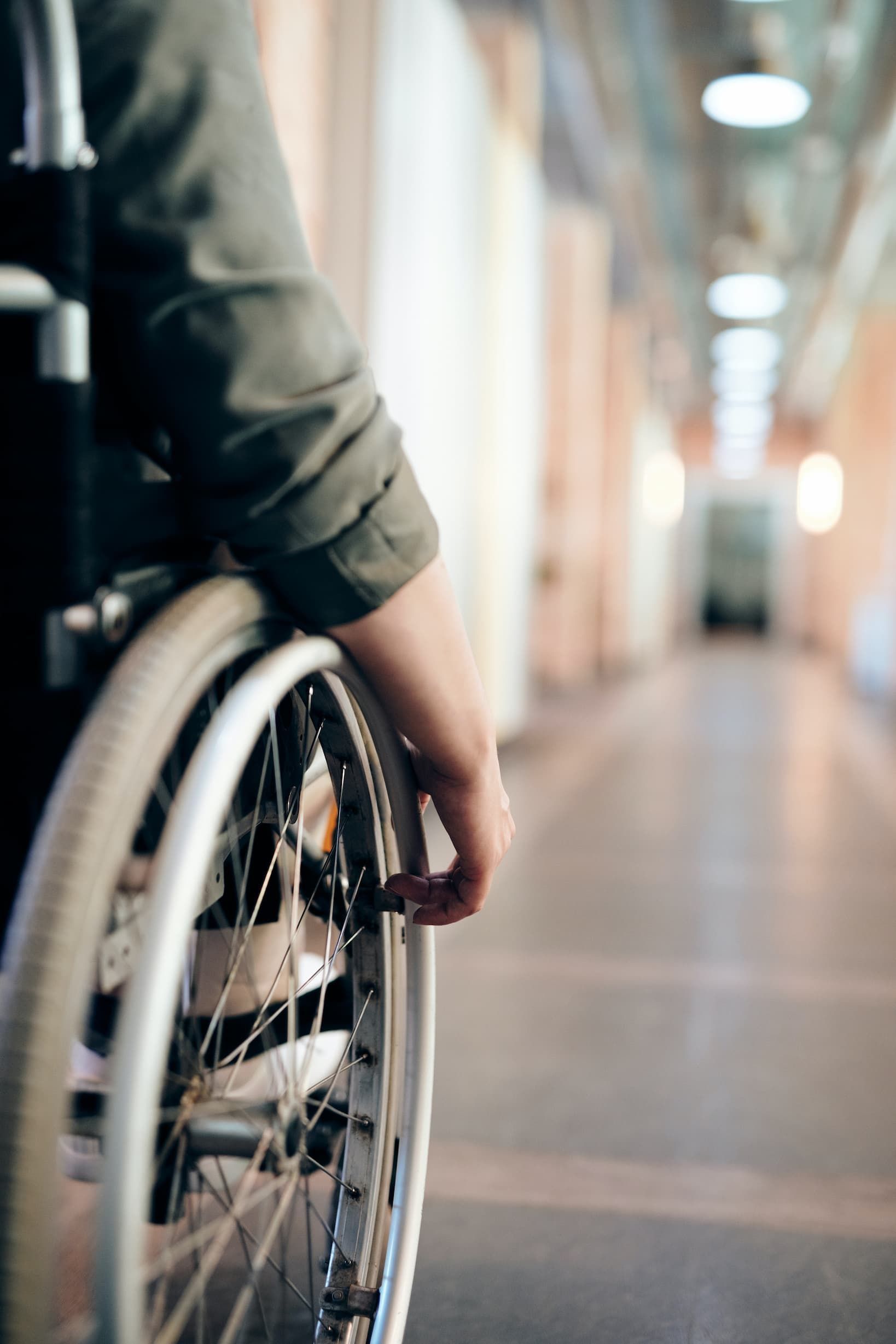 Person in wheelchair in a hallway, hand on wheel.