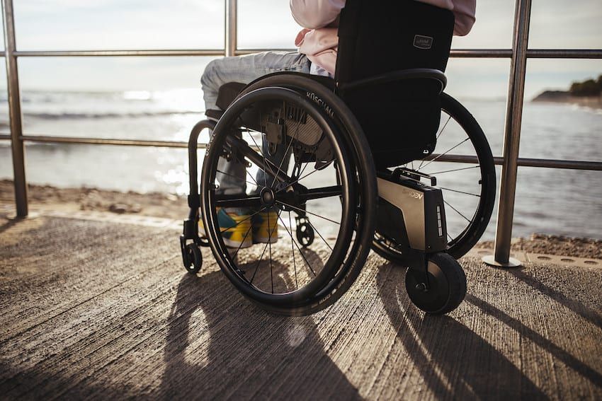 Wheelchair with a black seat and a black storage bag. The wheels are silver with green accents.