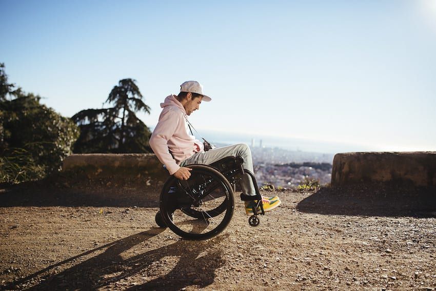 Wheelchair with a black seat and a black storage bag. The wheels are silver with green accents.