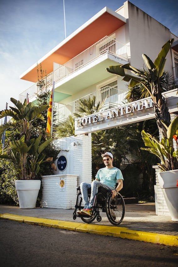 Wheelchair with a black seat and a black storage bag. The wheels are silver with green accents.
