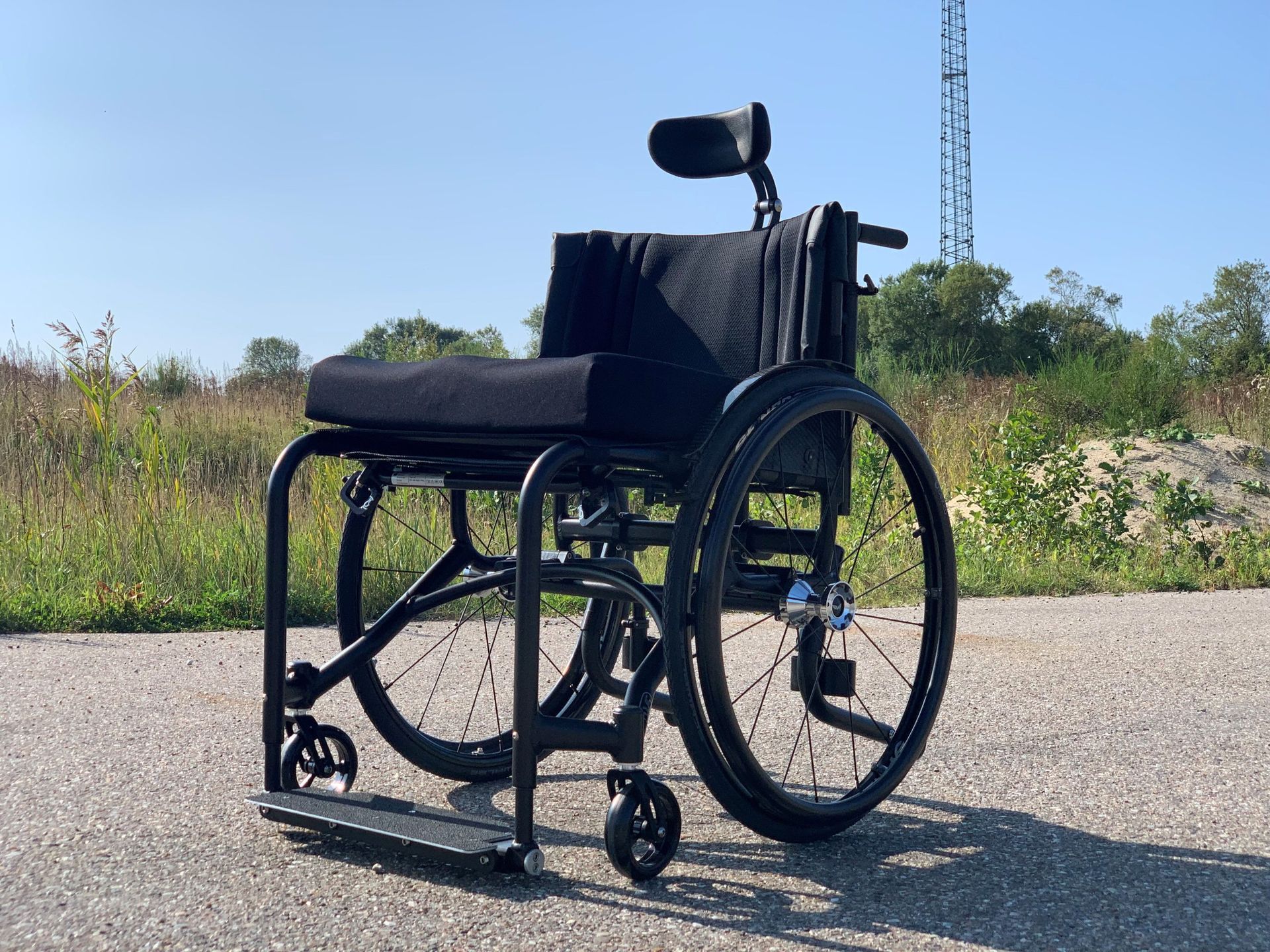 Black wheelchair with headrest on paved path, sunny day.