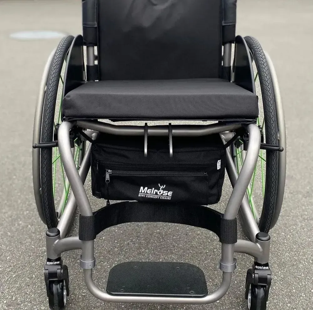 Wheelchair with a black seat and a black storage bag. The wheels are silver with green accents.