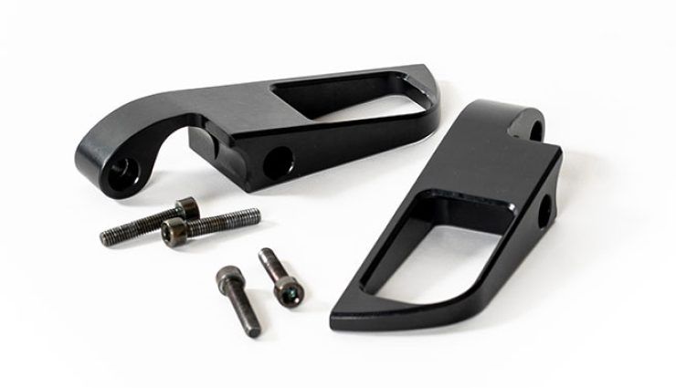 Black motorcycle foot peg brackets and mounting screws against a white backdrop.