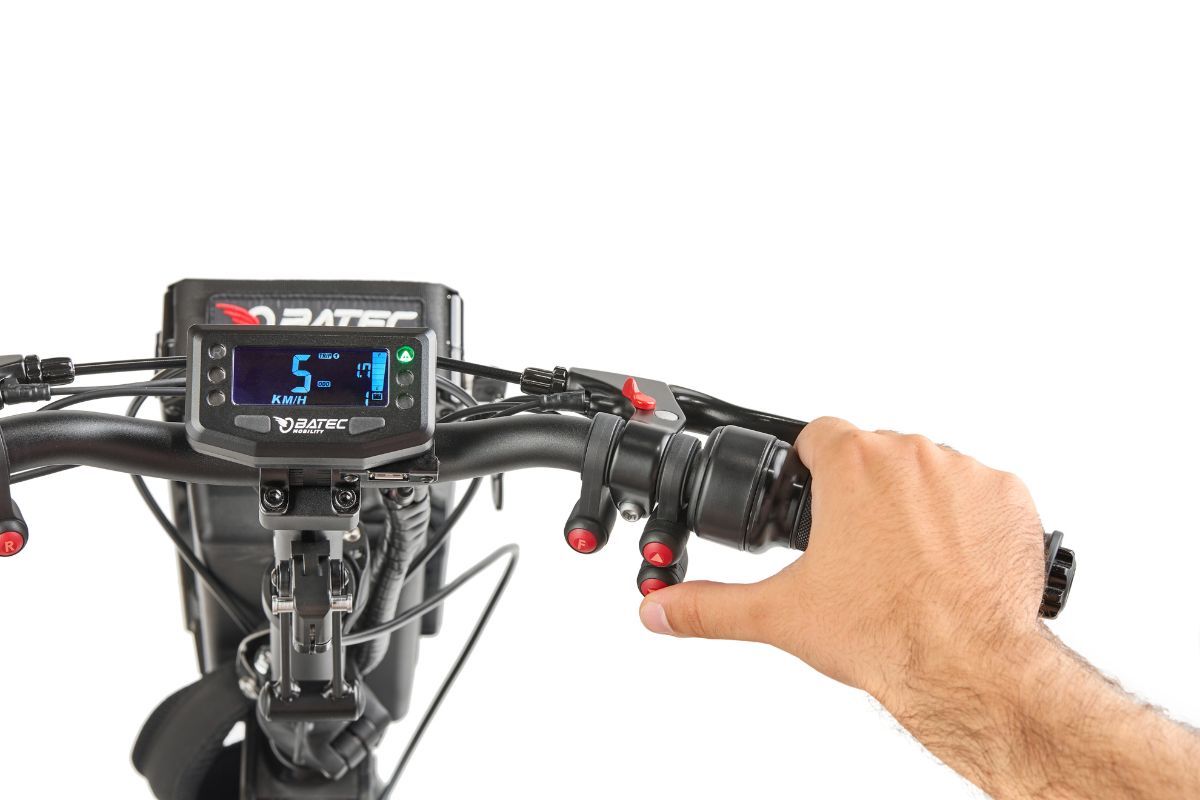 Person's hand on a scooter throttle, digital display shows speed, black handlebars with red buttons.