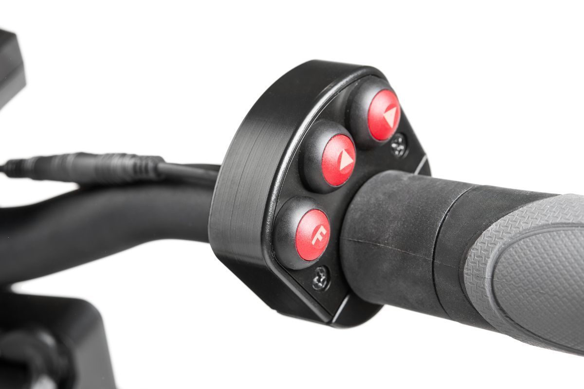 Close-up of a bicycle handlebar with a black control button cluster and red buttons
