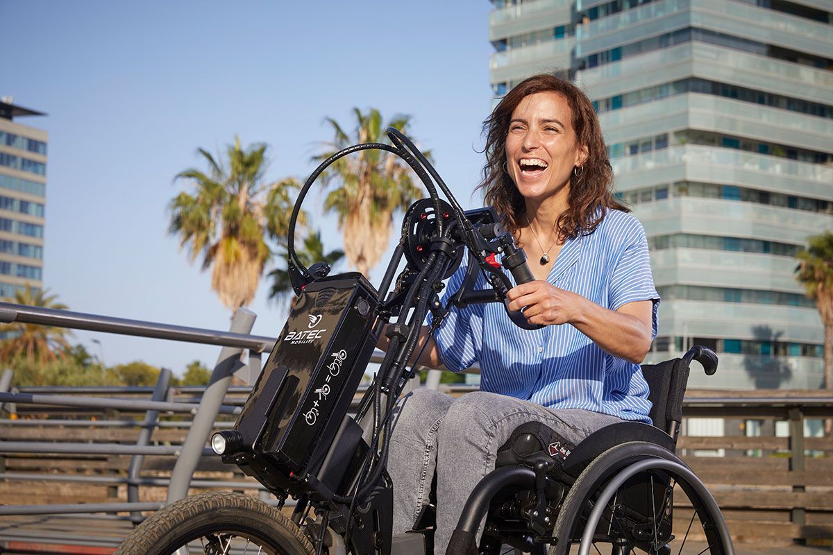 Woman in wheelchair smiles, operating a powered add-on. 