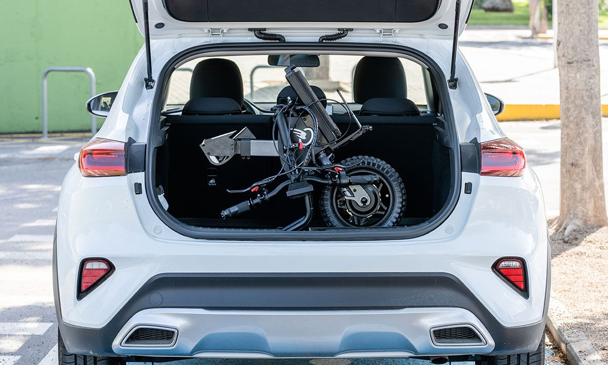 White SUV trunk open, a black folding wheelchair inside. Outdoors, parked next to a tree.