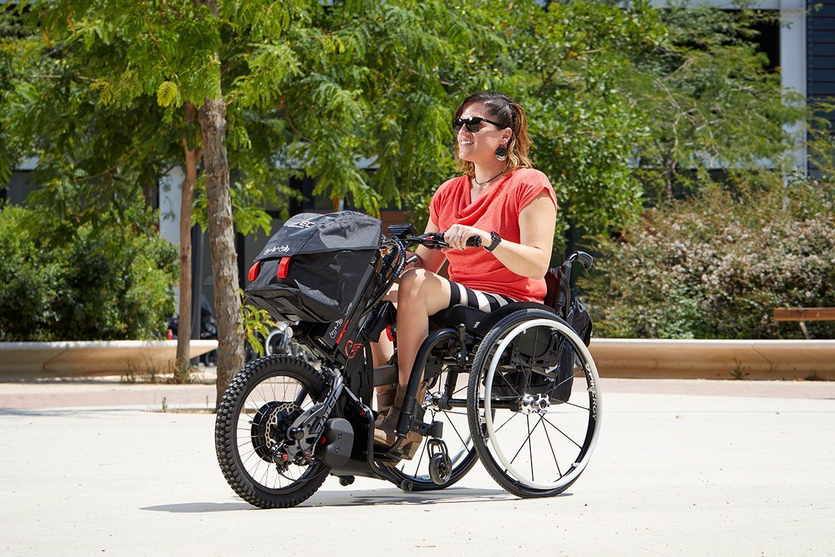 Woman in wheelchair driving a motorized attachment outdoors, sunny setting.