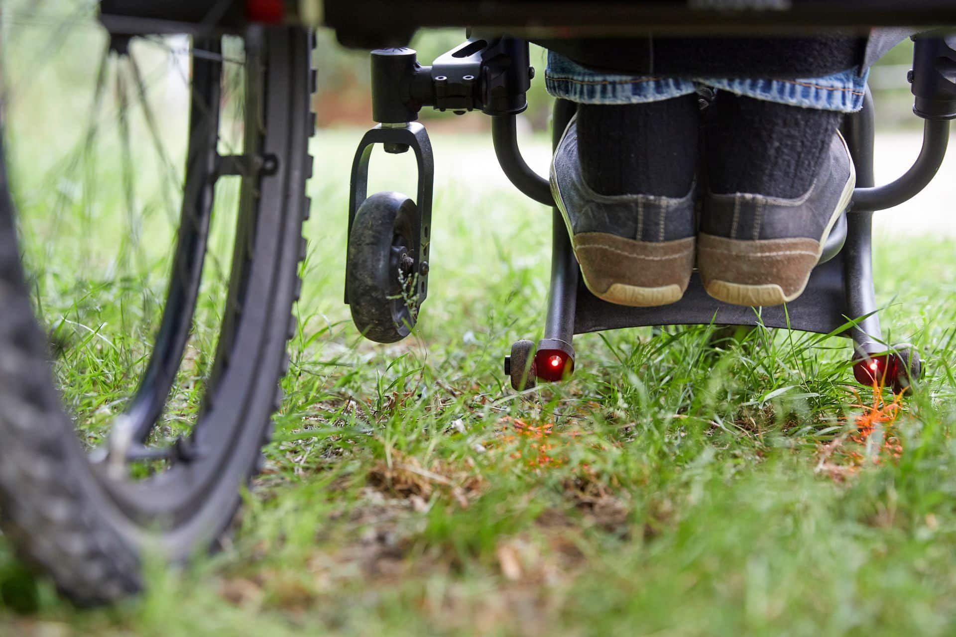 Person in a wheelchair outdoors on grass, with detail of shoes, back wheel, and footrest.