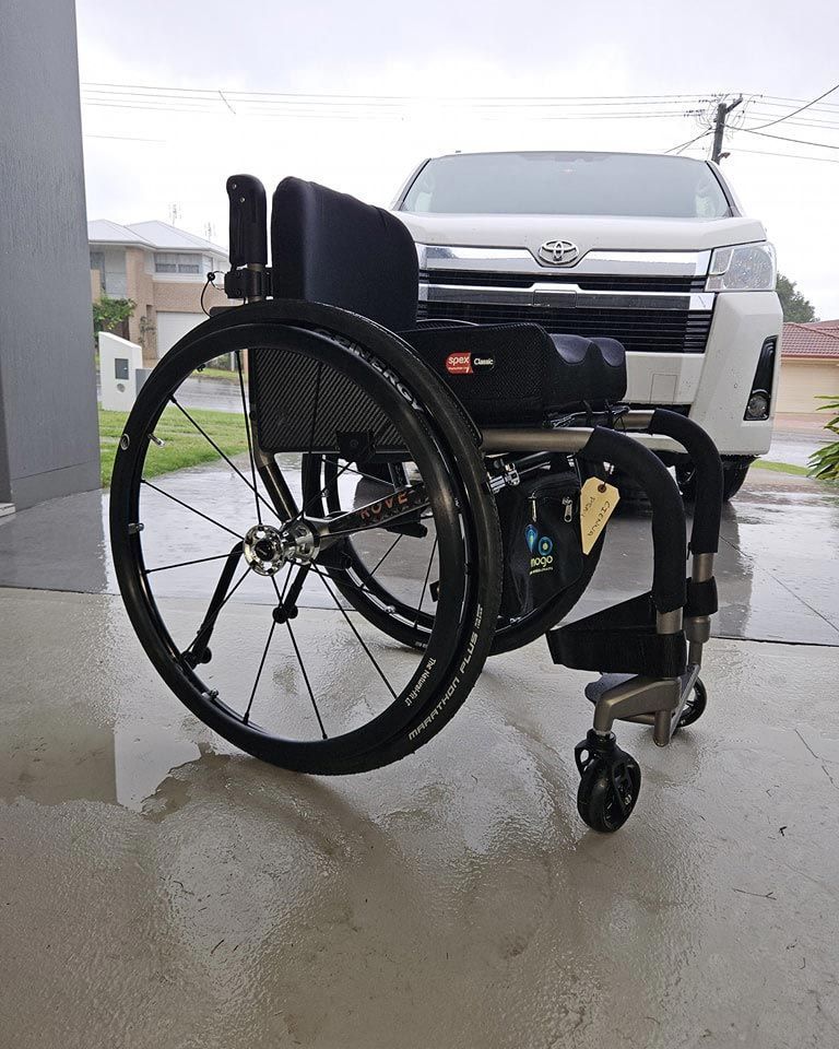 Wheelchair on wet pavement in front of a white van, on a cloudy day.