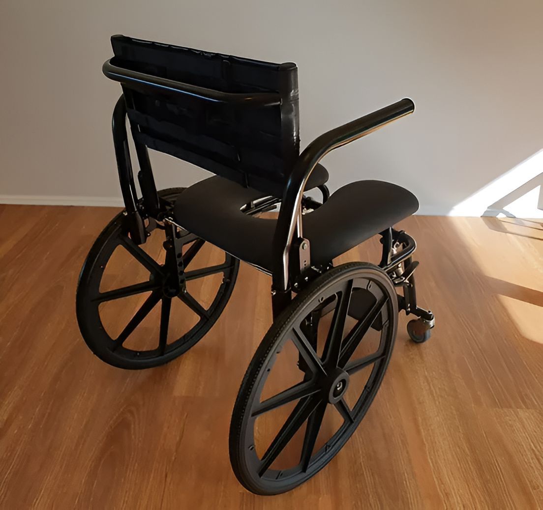 Black wheelchair on a wood floor in front of a white wall.