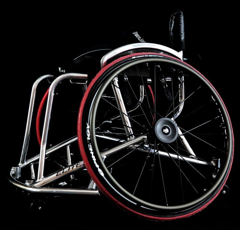 Silver wheelchair with red trim and black tires, set against a black background.