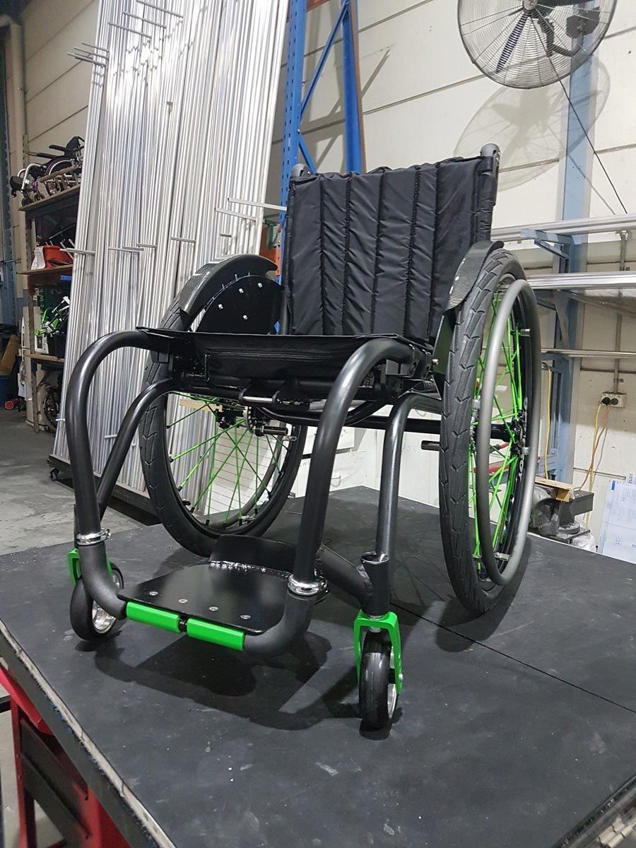Black and green wheelchair on a black surface; it is indoors in a workshop-type setting.