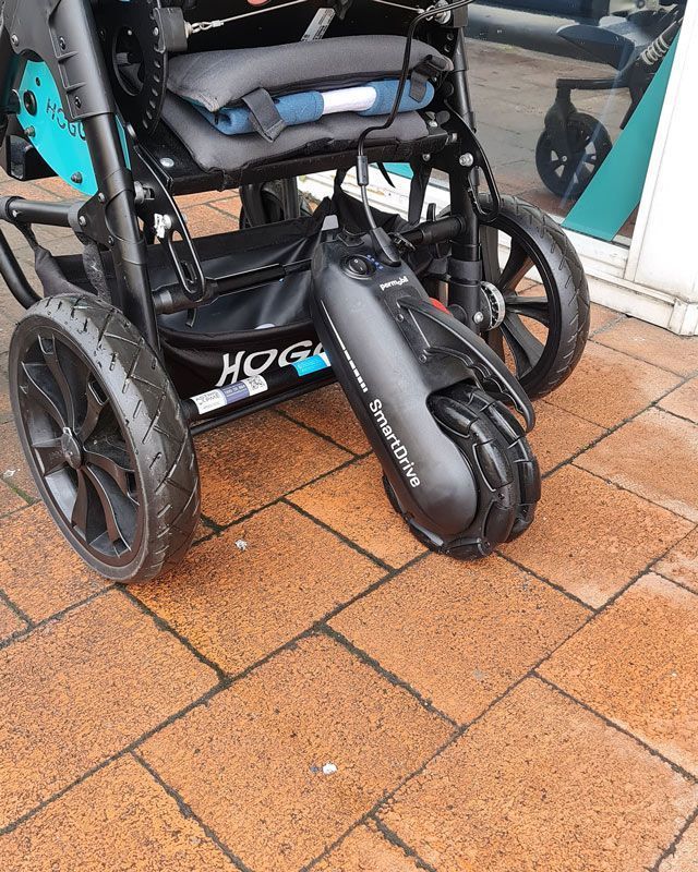 Black wheelchair with an attached SmartDrive power assist on a brick surface.