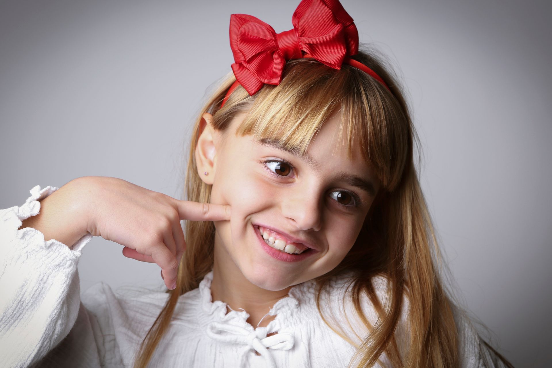 A little girl with a red bow on her head is smiling.