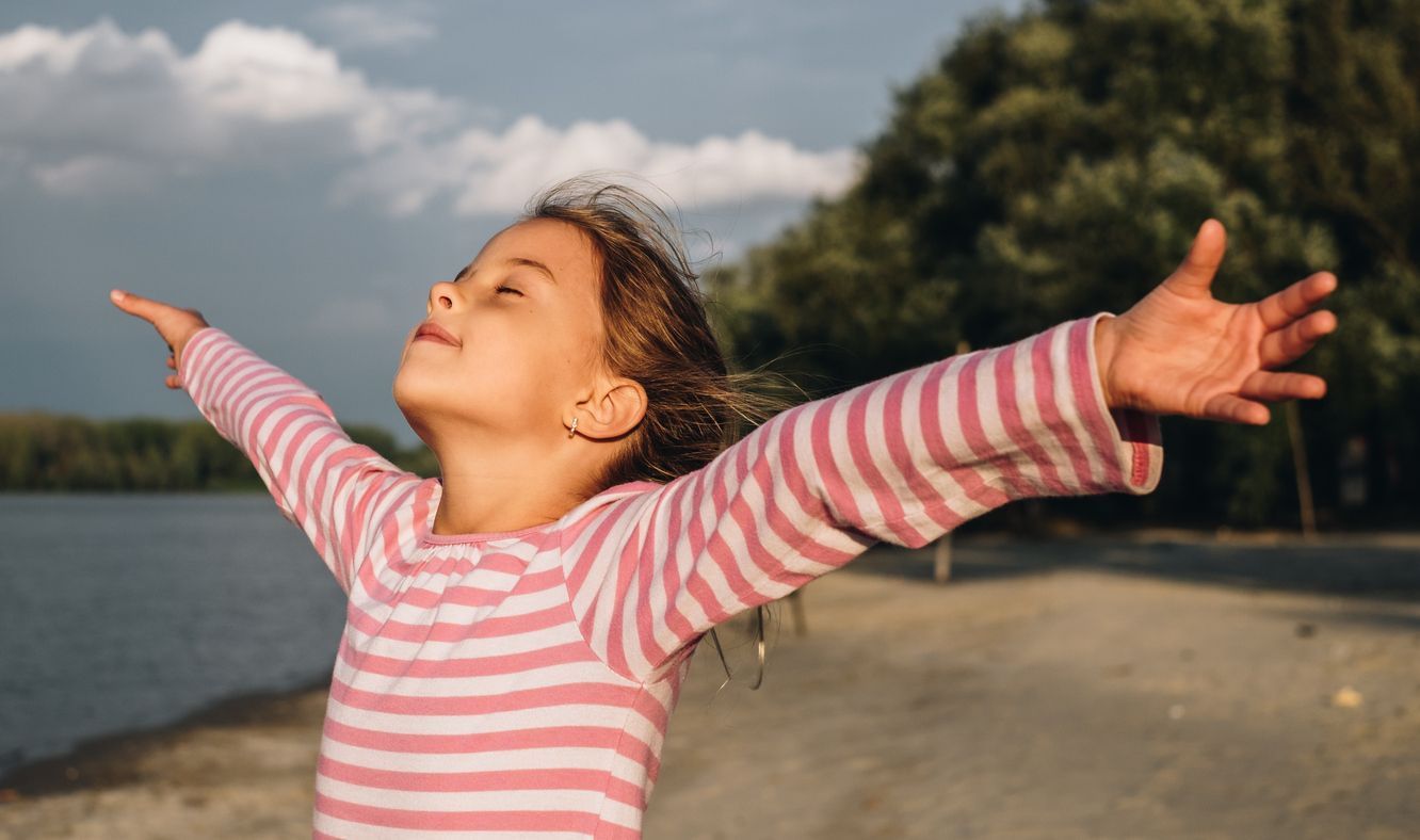 A little girl is standing on a beach with her arms outstretched.