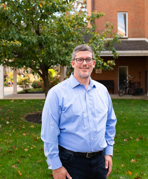 Man in glasses, blue shirt, standing in front of building and tree, smiling | Brad Reigner Lancaster, PA CPA