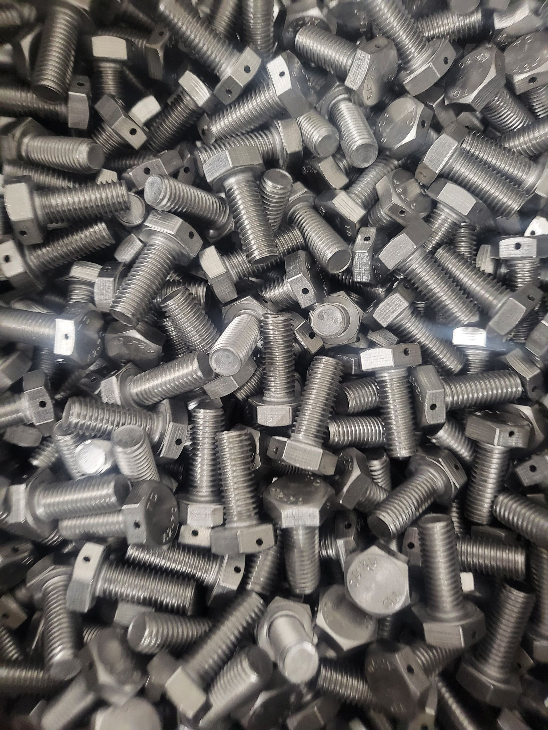 Pile of shiny, silver bolts with hexagonal heads, tightly packed together.