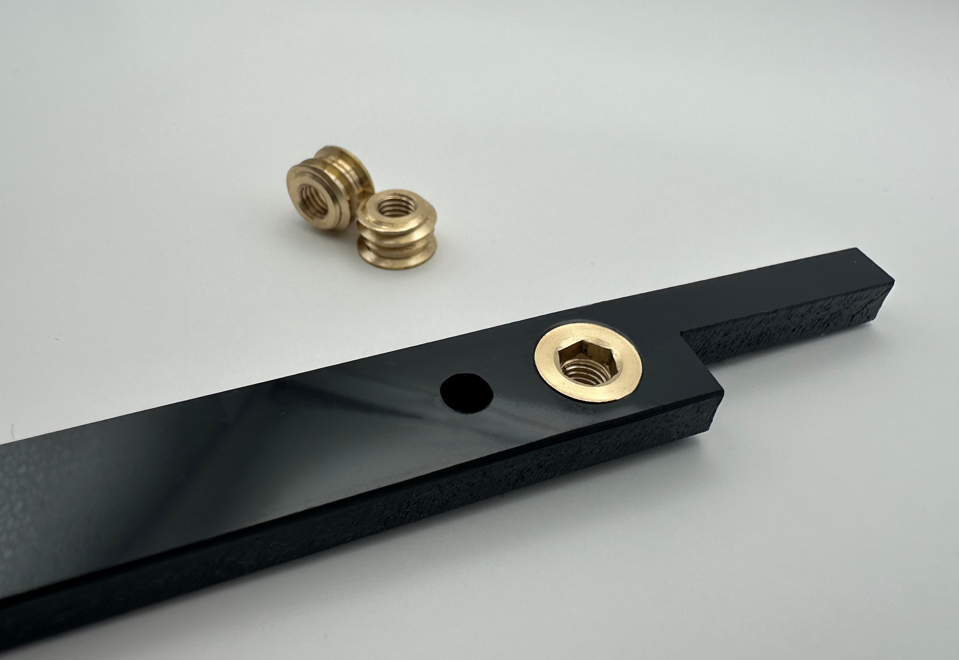 Black plastic bar with brass inserts and two loose brass inserts on a white surface.