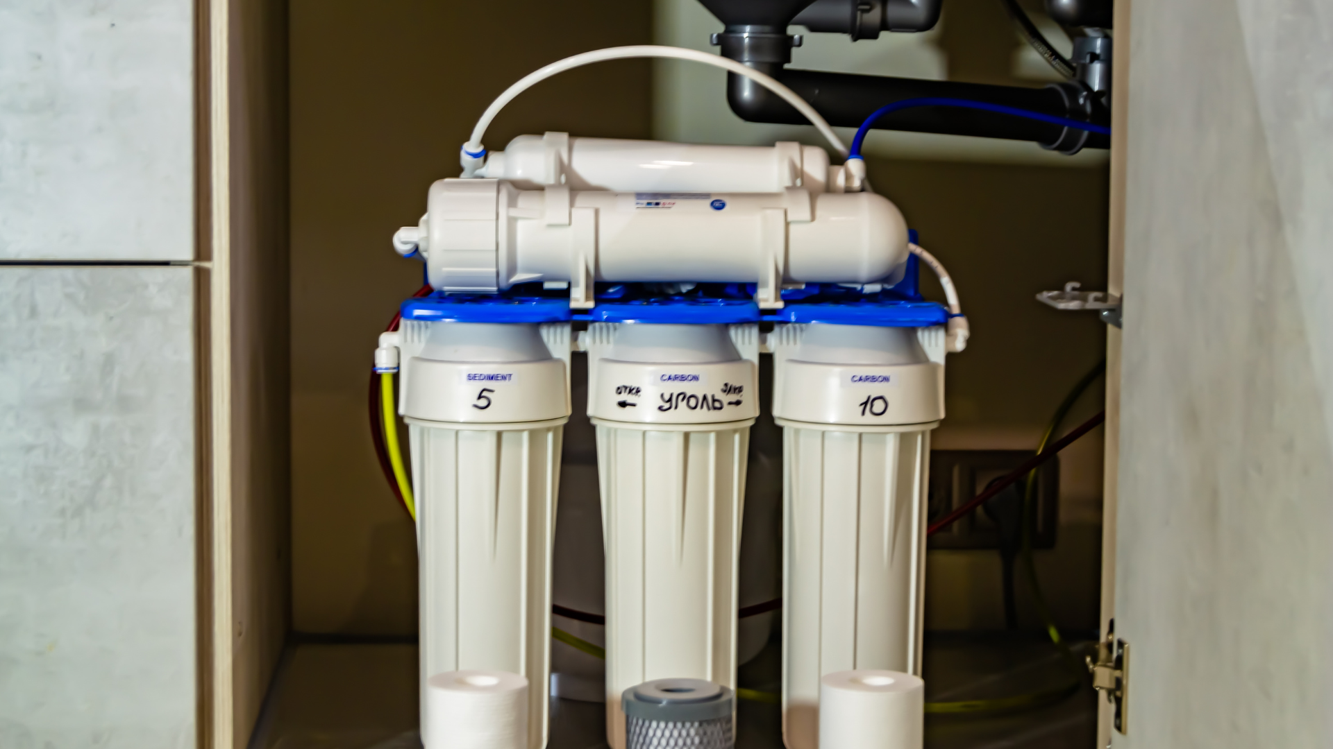 Water filtration system with white and blue components, inside a cabinet.