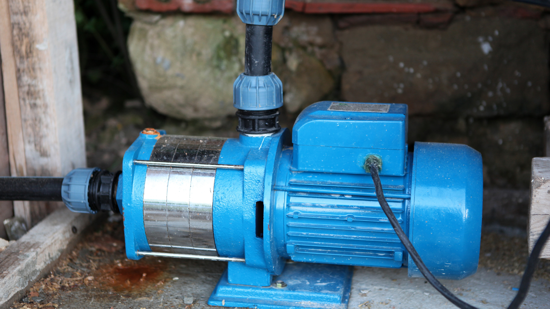 Blue water pump with black and blue pipes connected, sitting on a wooden base.