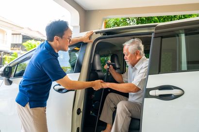 Man helping elderly passenger into a white van through the open side door