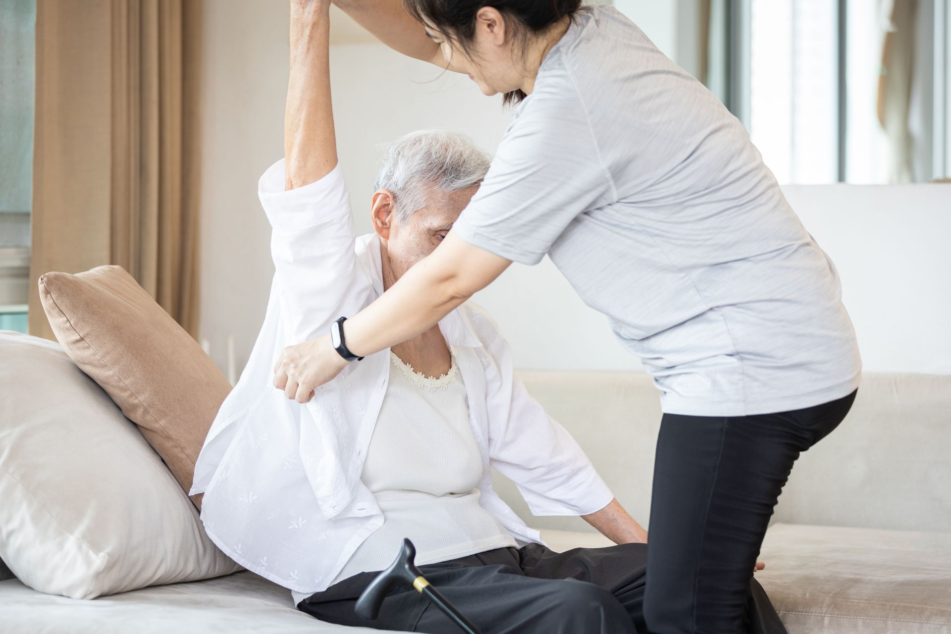 Caregiver helping an elderly person sit up on a bed in a bright room Caregiver helping an elderly person sit up on a bed in a bright room
