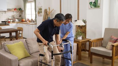 Person using a walker with caregiver support in a bright living room