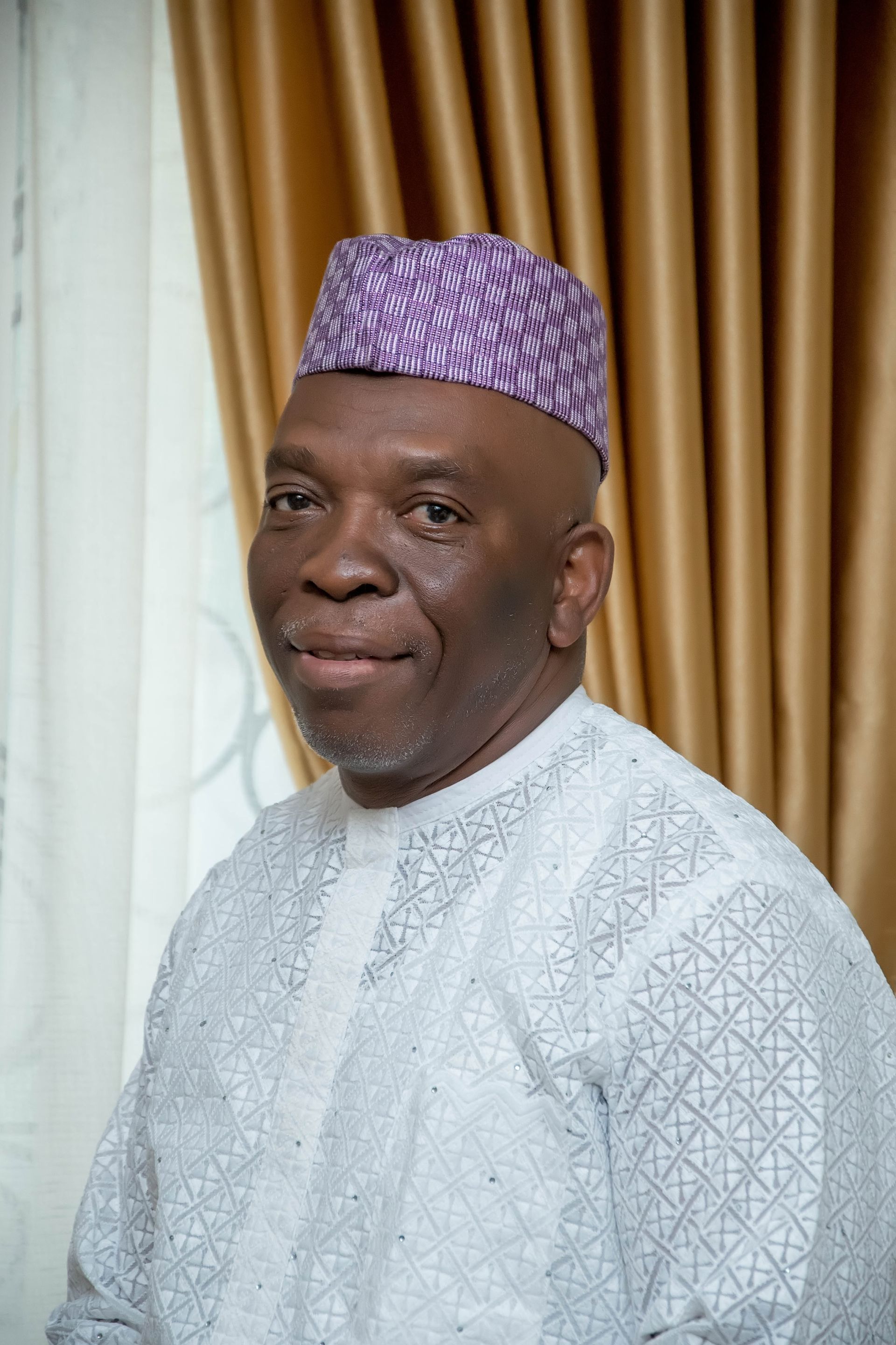 A man wearing a purple hat and a white shirt is standing in front of a window.