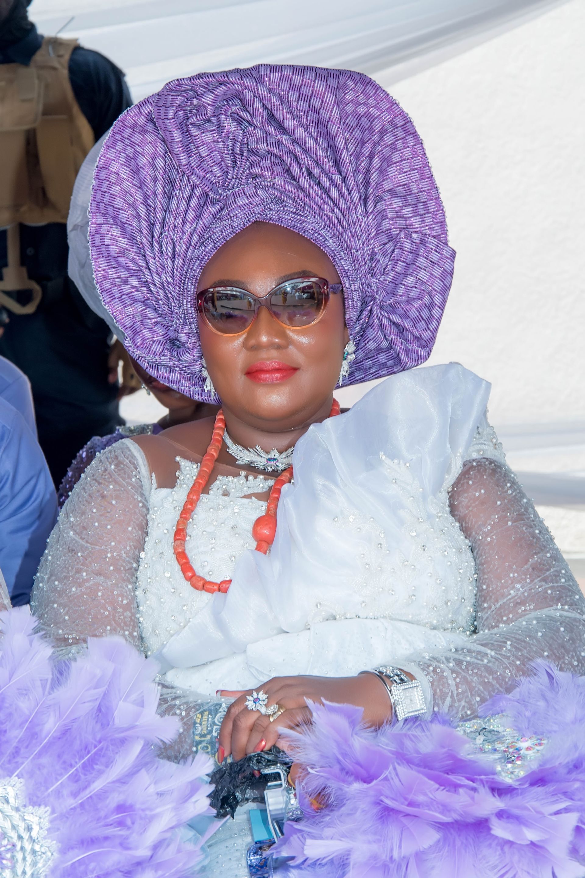A woman wearing a purple turban and sunglasses is sitting down.