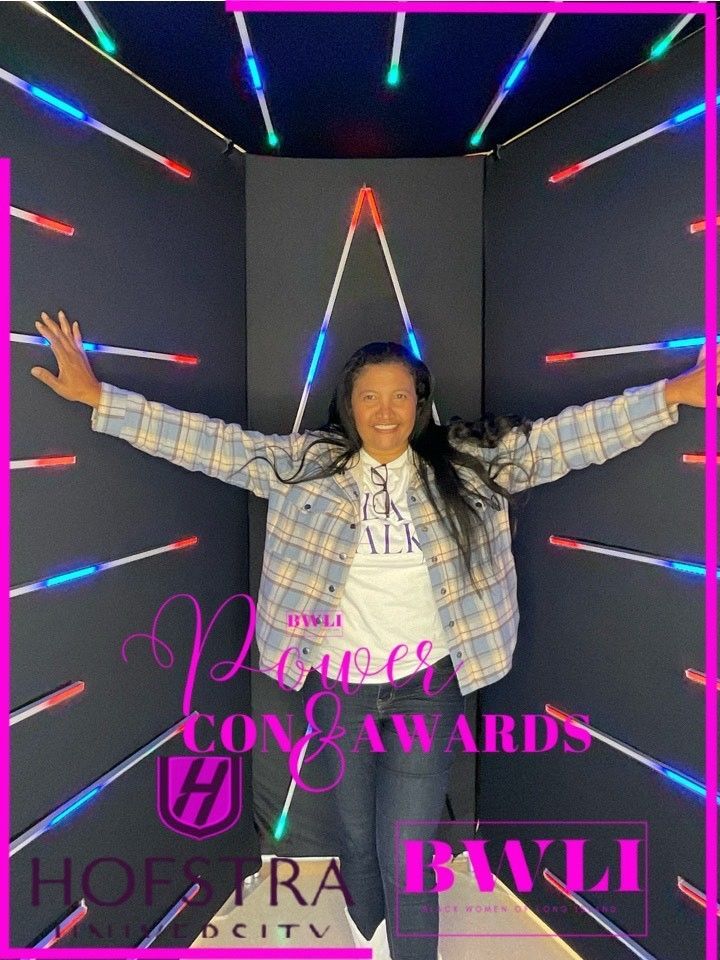 A woman in a plaid shirt is standing in a dark room with her arms outstretched.